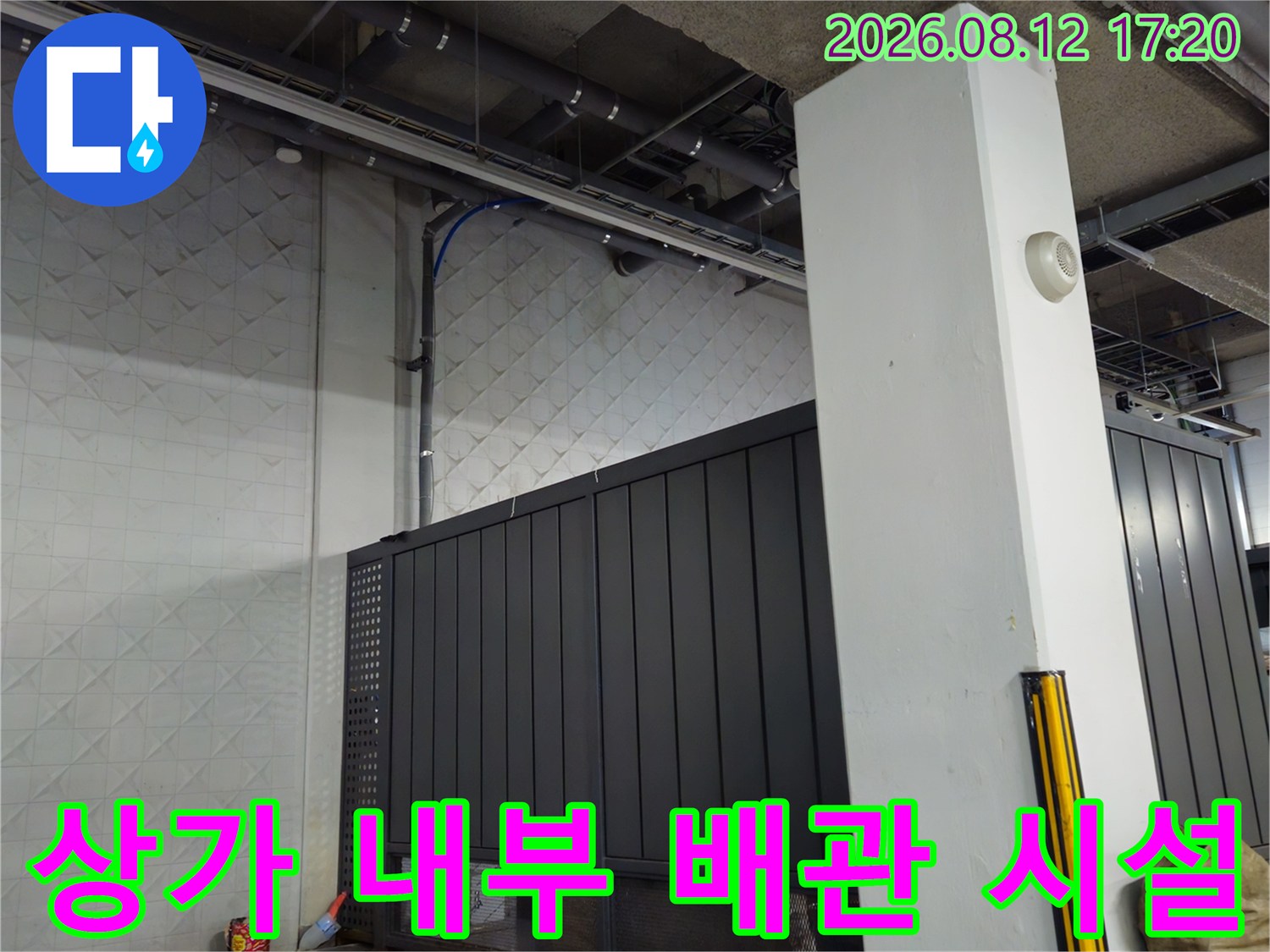 상가 지하주차장의 벽면 타일과 상단에 설치된 배관 설비의 모습입니다.