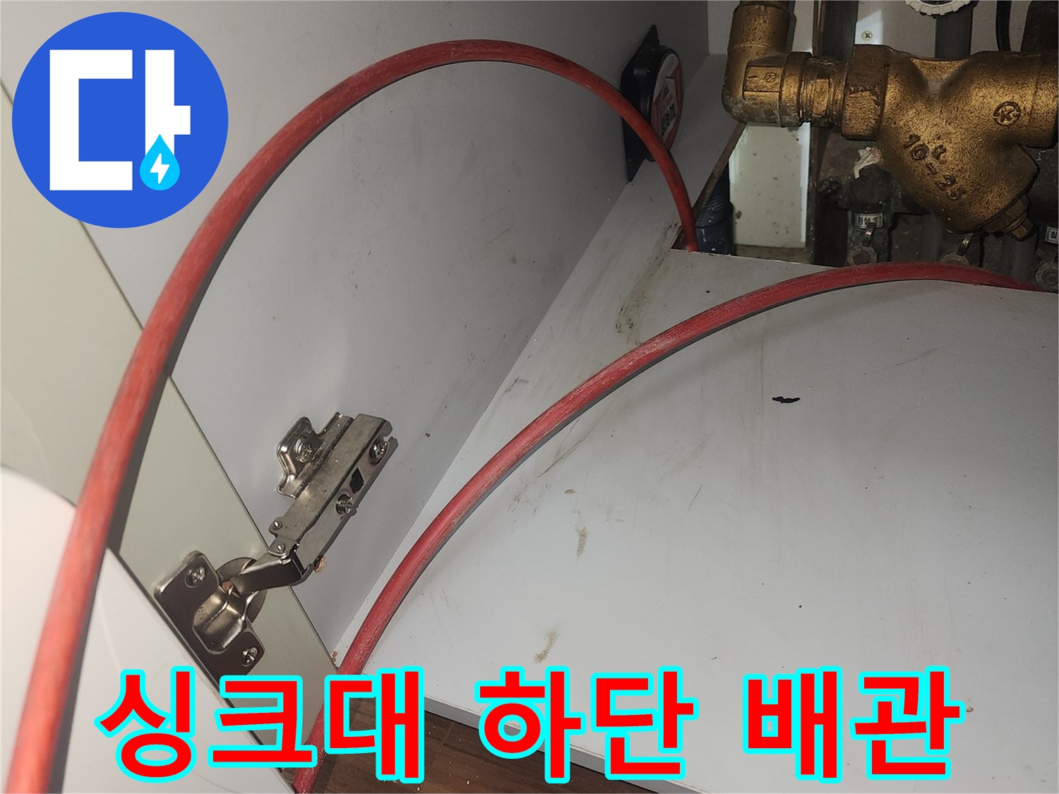 금속 재질의 수전 배관과 붉은색 호스가 지나가는 주방 하부 모습