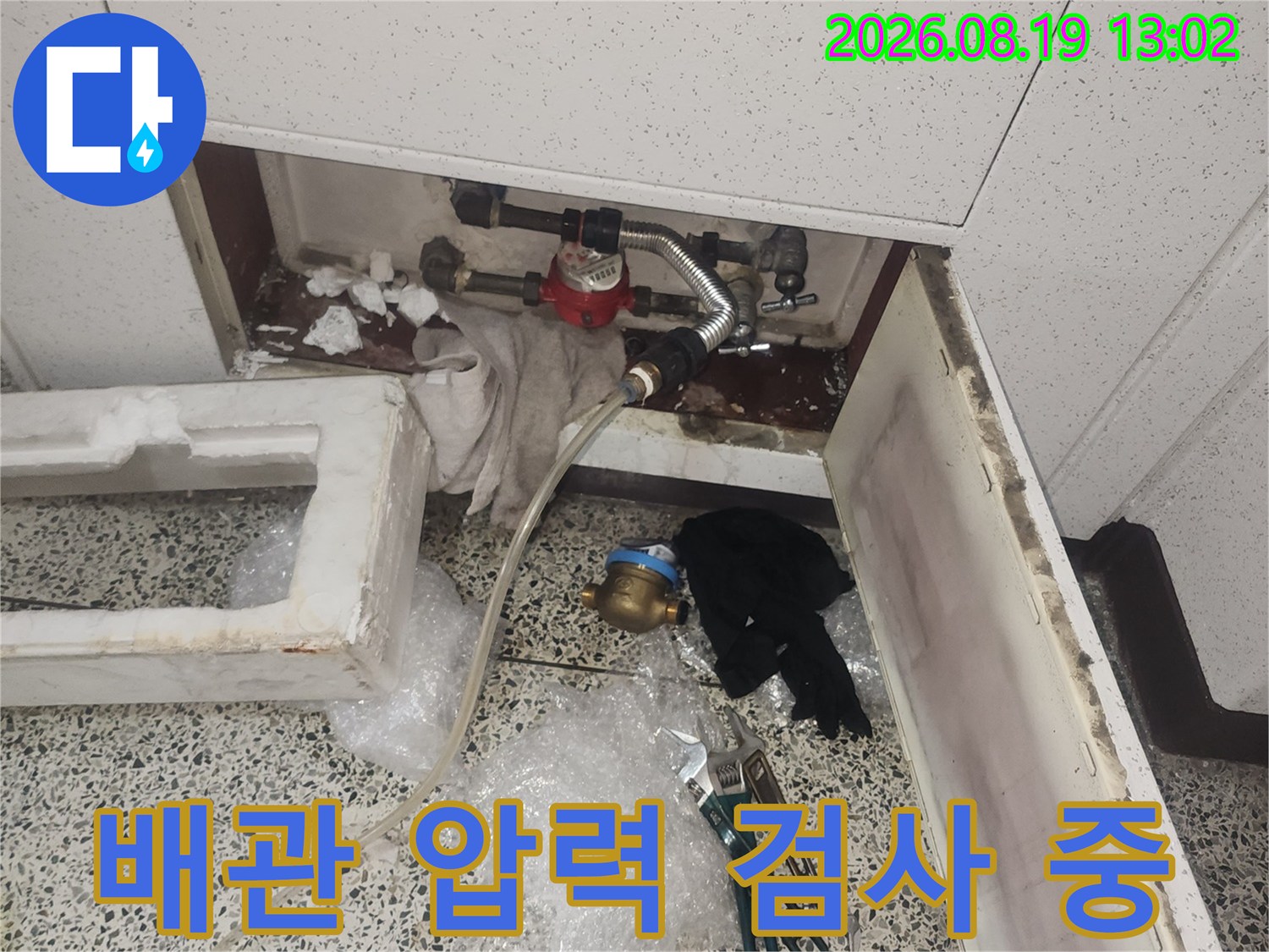 싱크대 하부의 금속 배관과 밸브에 연결된 공압 검사 장비 모습입니다.