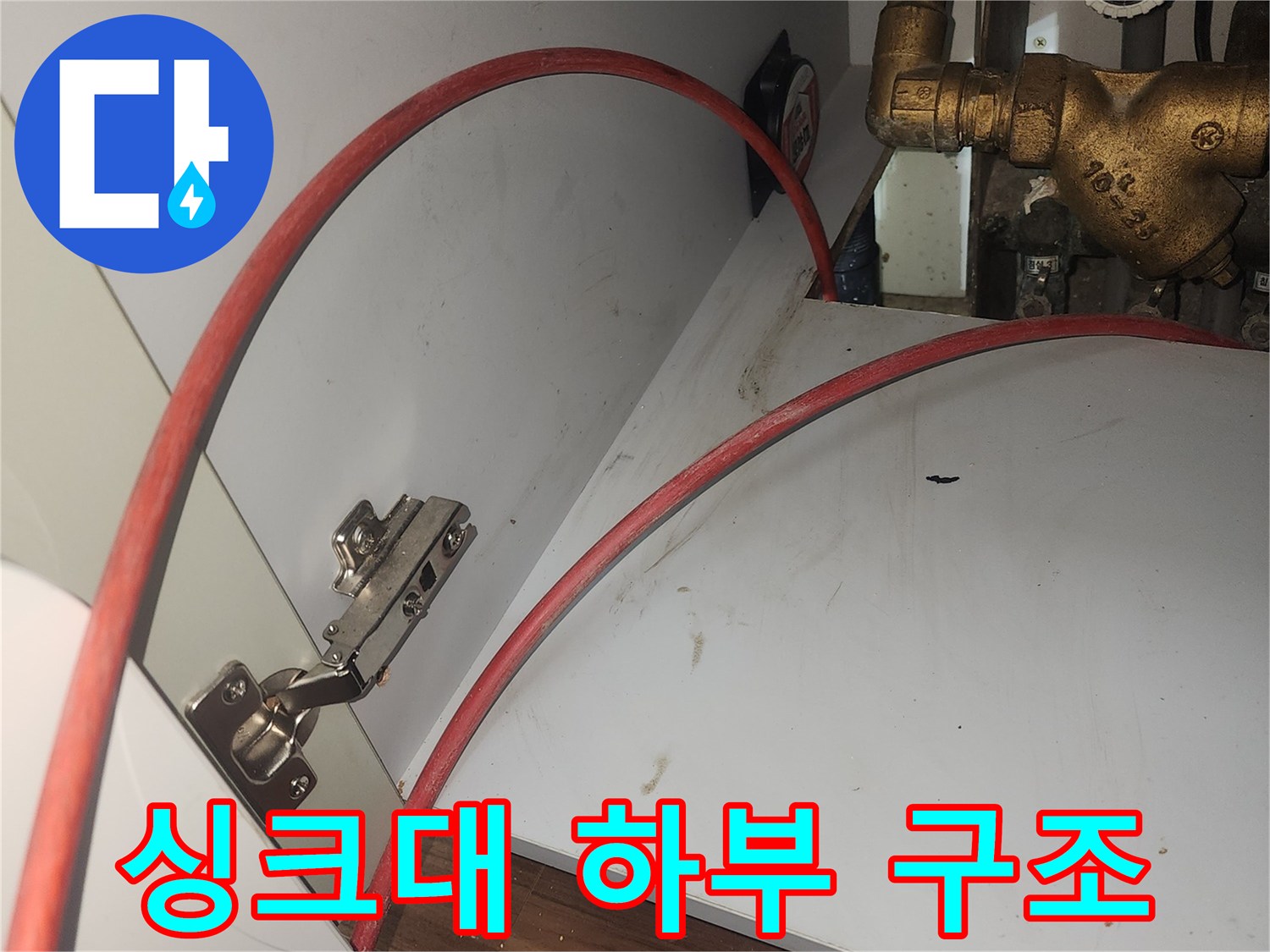 주방 싱크대 아래쪽 금속 수전과 붉은색 급수 호스 연결 부위