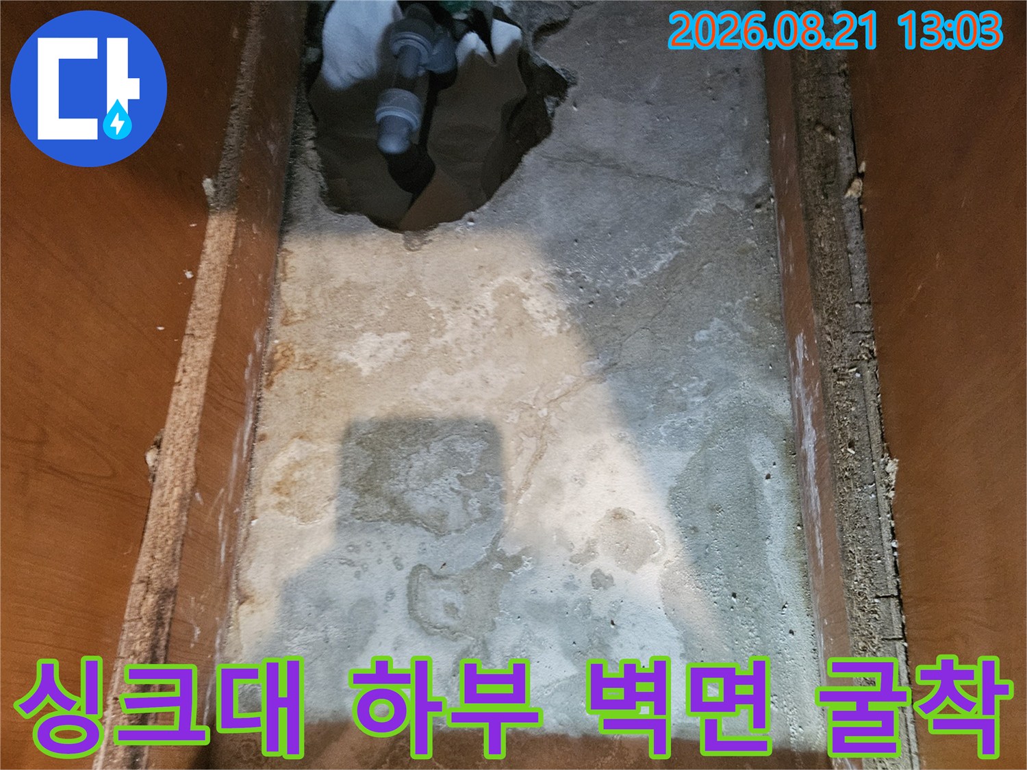 싱크대 아래쪽 콘크리트 벽을 파내어 드러난 배관과 젖은 벽면