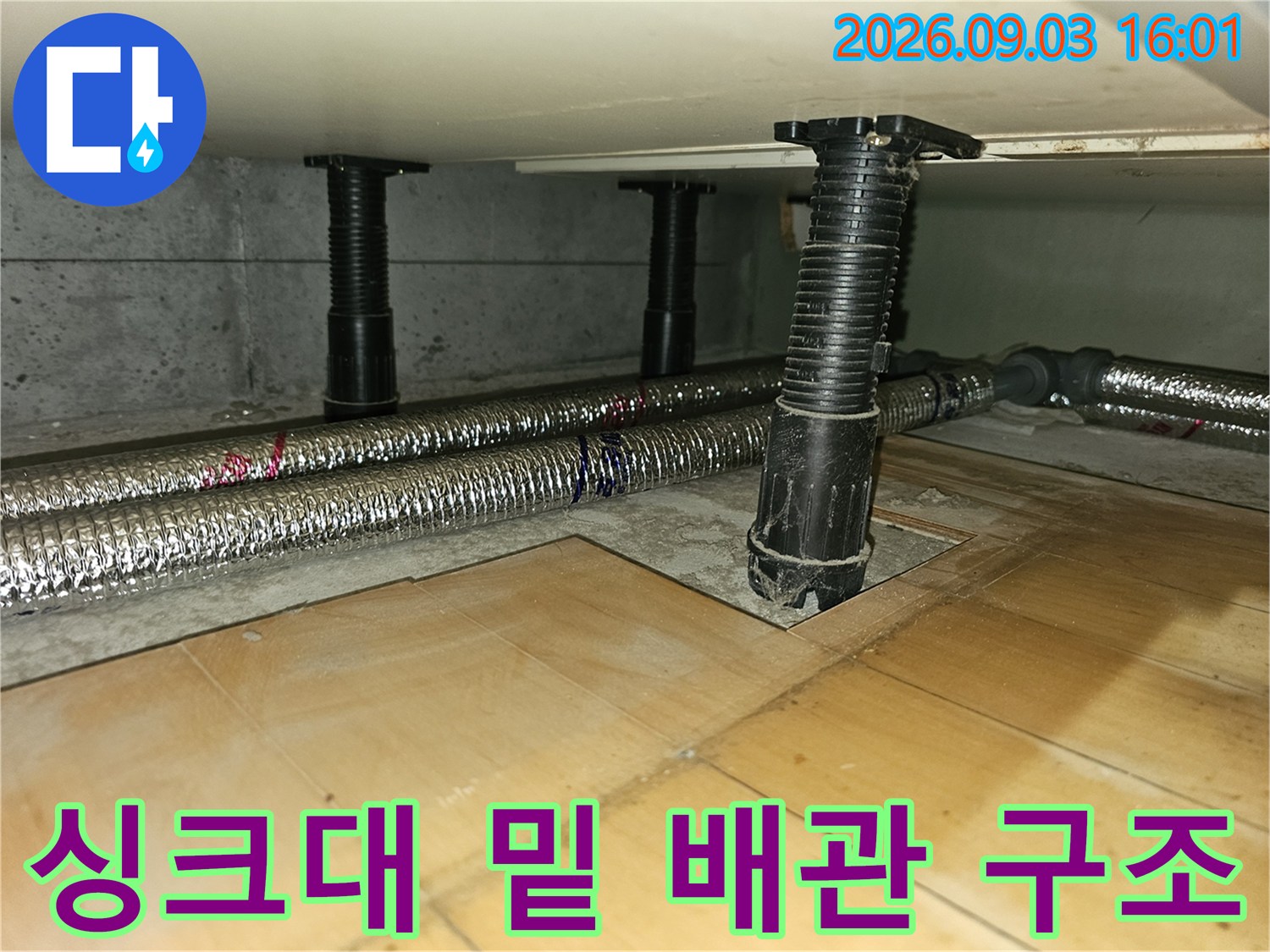 싱크대 하부 공간에 배치된 은색 보온 배관과 검은색 지지 기둥