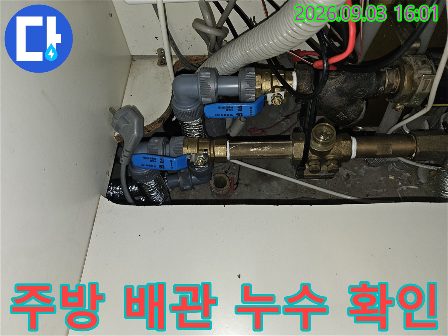 싱크대 하부 공간에 설치된 파란색 밸브와 금속 배관의 근접 촬영