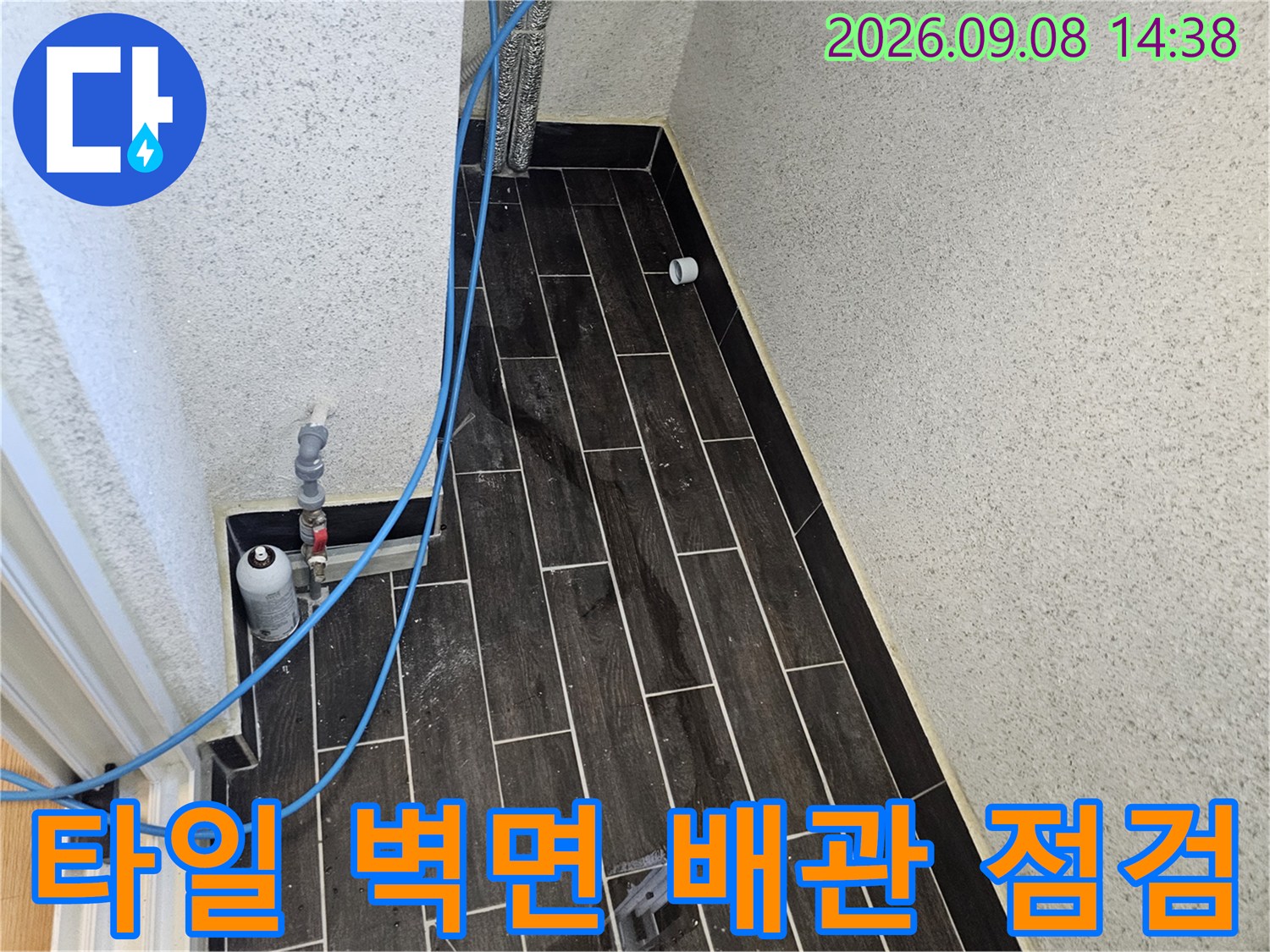 어두운 톤의 타일벽-압력 테스트를 위해 연결된 파란색 호스와 밸브 부속품