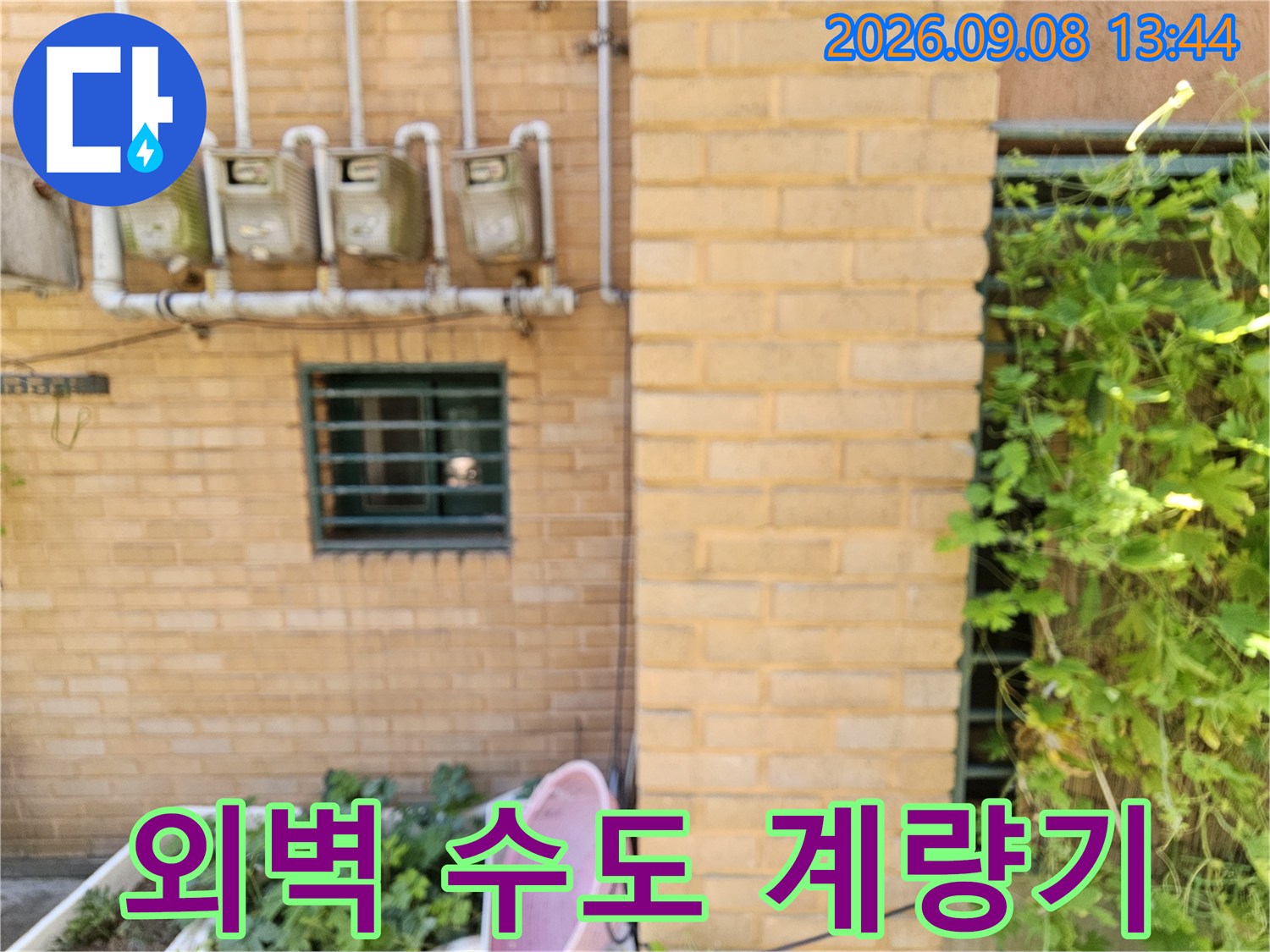 건물 외벽 벽돌 사이에 설치된 수도 계량기와 연결 배관 모습입니다.