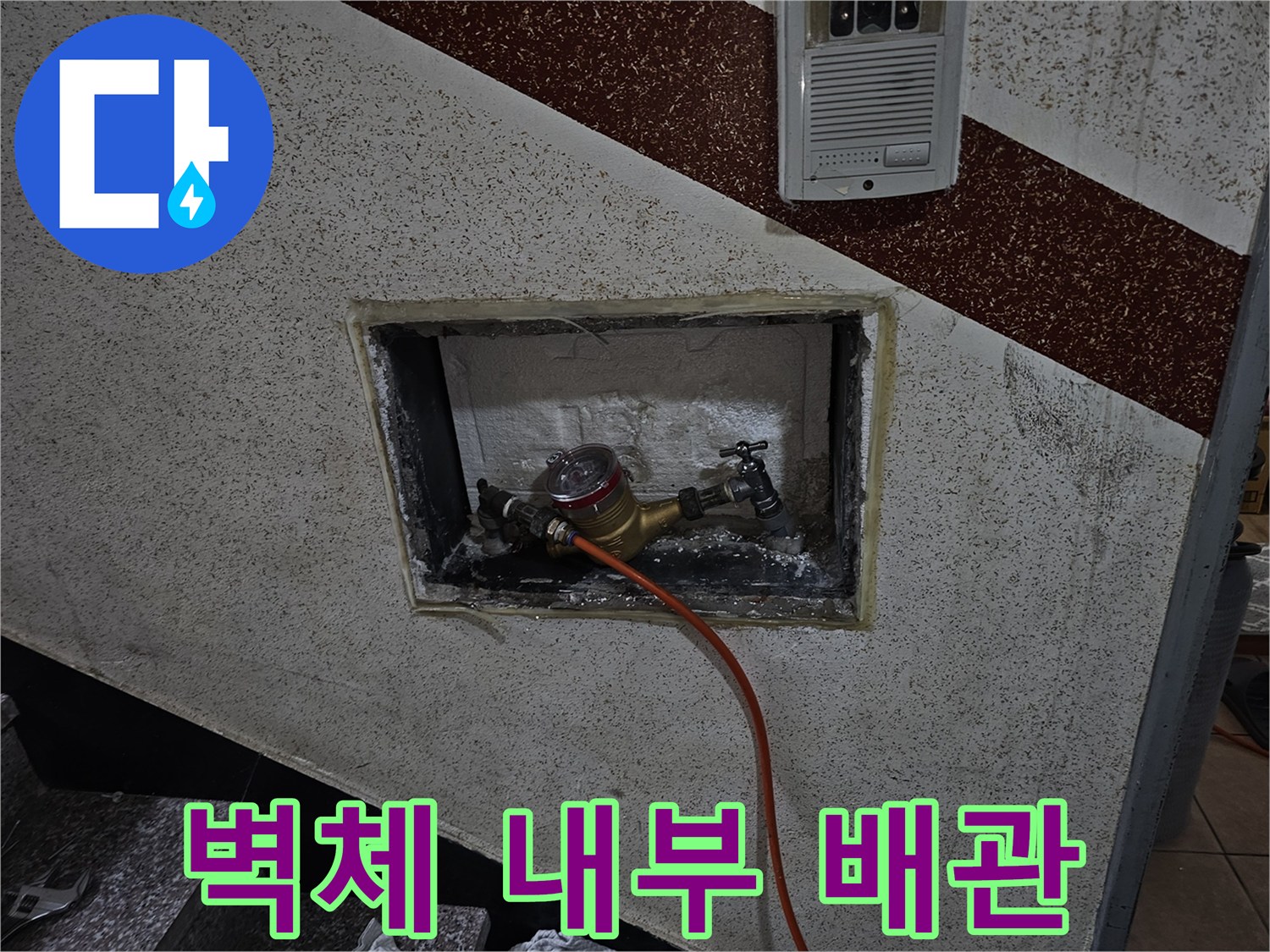 타일 뒤편에 노출된 금색 배관과 주황색 호스 연결부