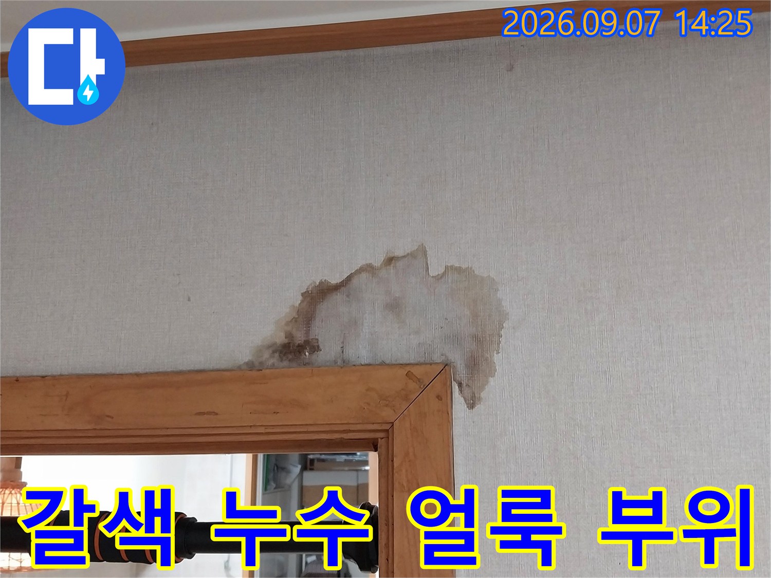 문틀 옆 벽지에 발생한 짙은 갈색의 물자국 사진입니다.