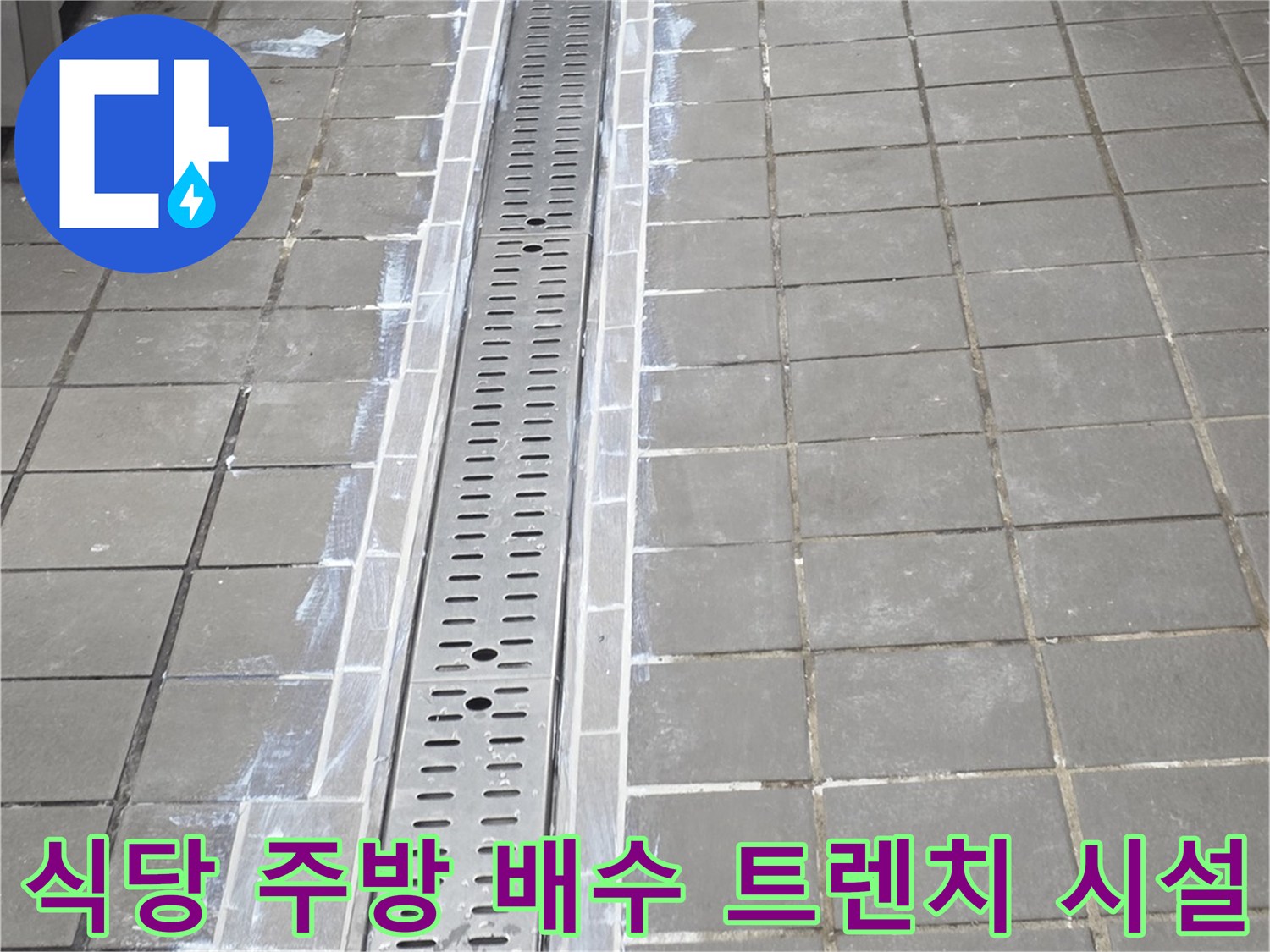 스테인리스 소재의 배수 트렌치가 설치된 주방 바닥 타일 모습입니다.