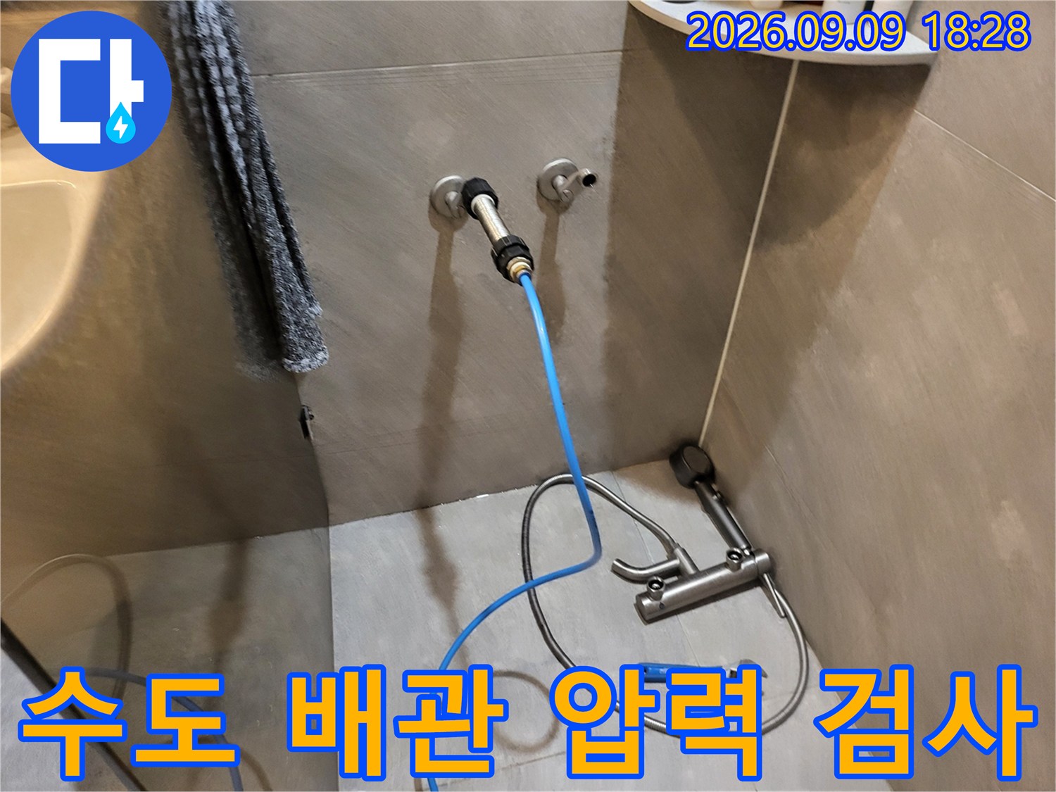욕실 벽면 수도 밸브 부근에 연결된 파란색 공압 테스트 호스 상세 모습입니다.