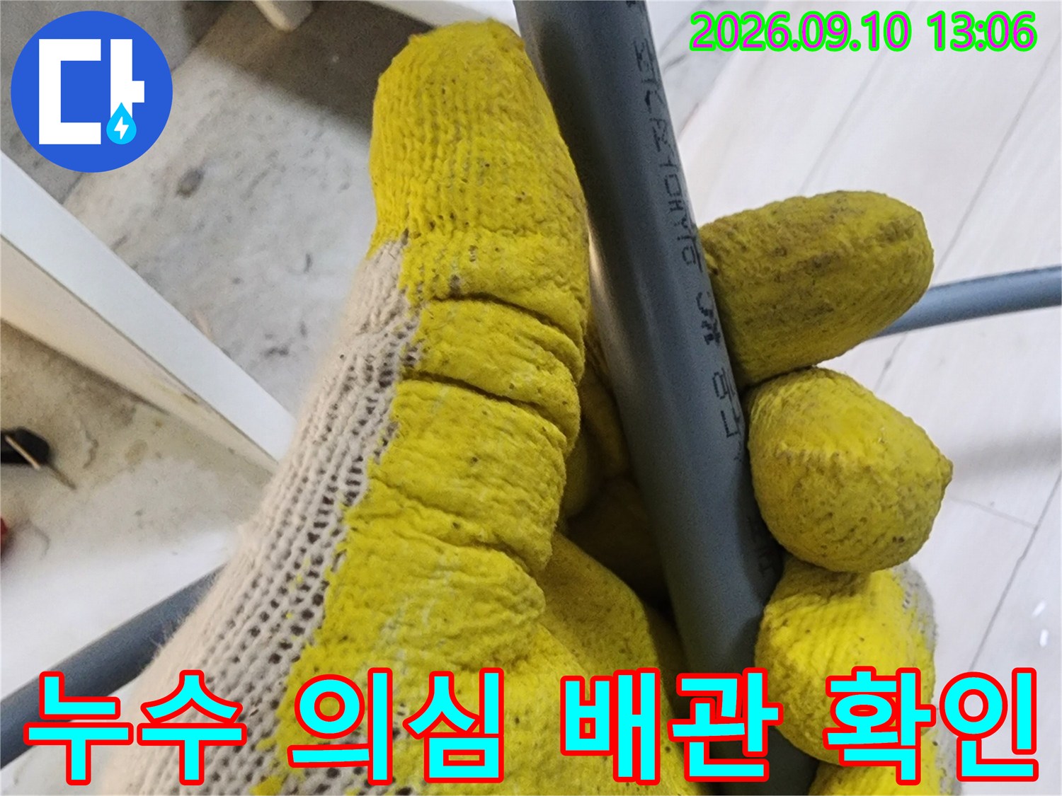 노란 장갑을 낀 작업자가 회색 배관의 연결 상태를 면밀히 관찰합니다.