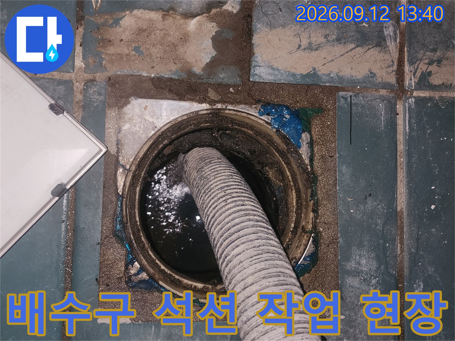 세탁실 배수구 내부의 고인 물을 제거하기 위해 석션 장비를 사용하는 모습입니다.
