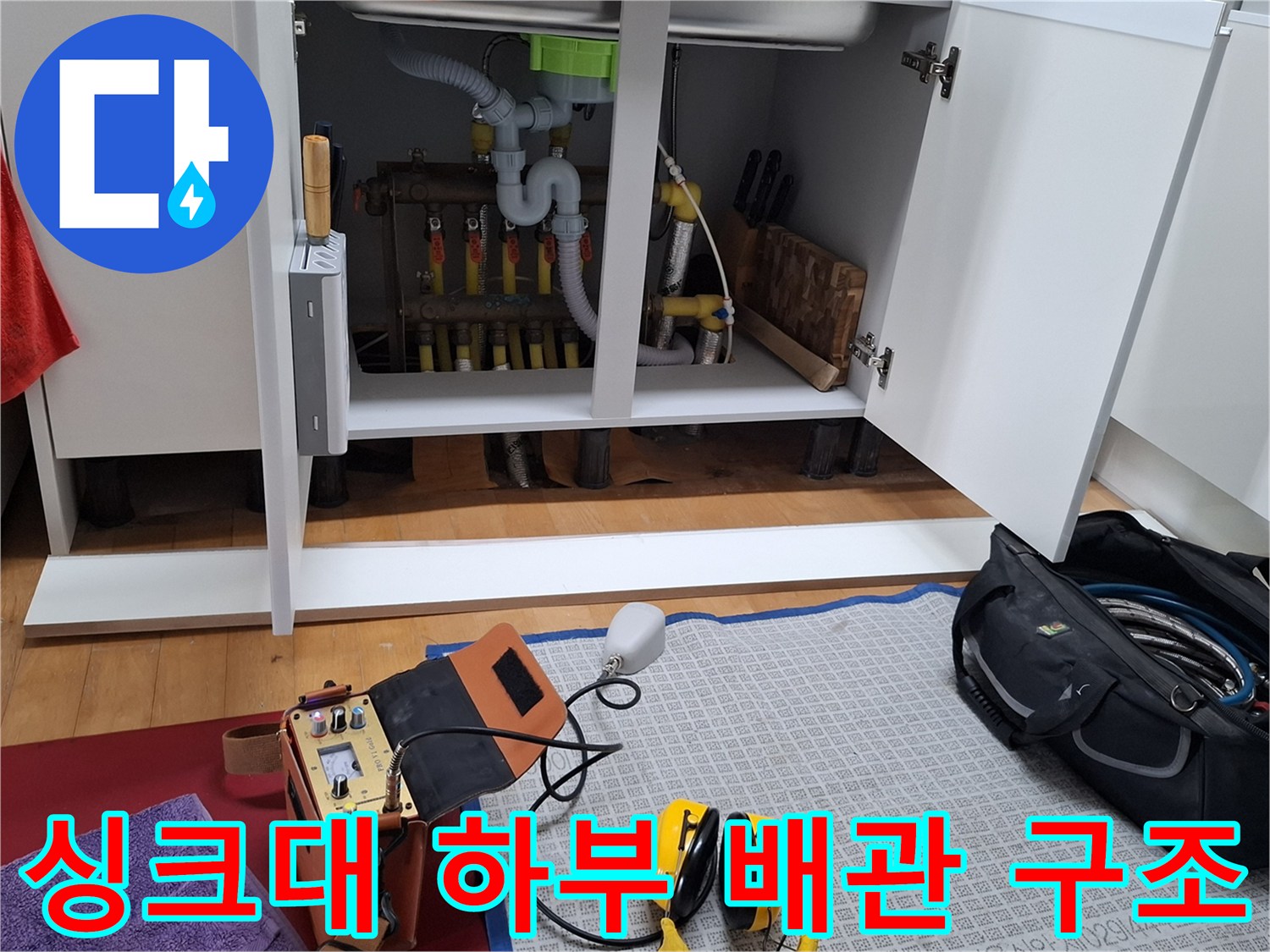 싱크대 밑에 복잡하게 연결된 난방 분배기와 노란색 엑셀 파이프들