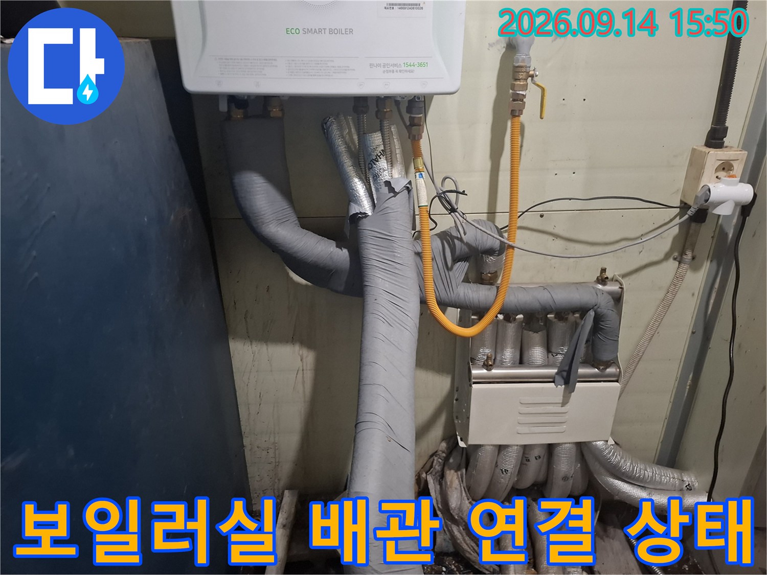 회색 보온재가 씌워진 배관들이 분배기와 연결된 보일러실 내부 전경입니다.
